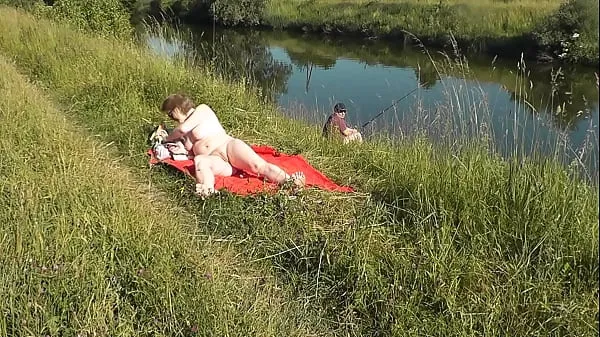 Hot MILF sexy Frina on river bank undressed and sunbathes naked. Random man fisherman watching for her, and in the end decided to join naked woman. Wild beach. Nudist beach. Public nudity. Public exposure. Naked in public วิดีโอใหม่